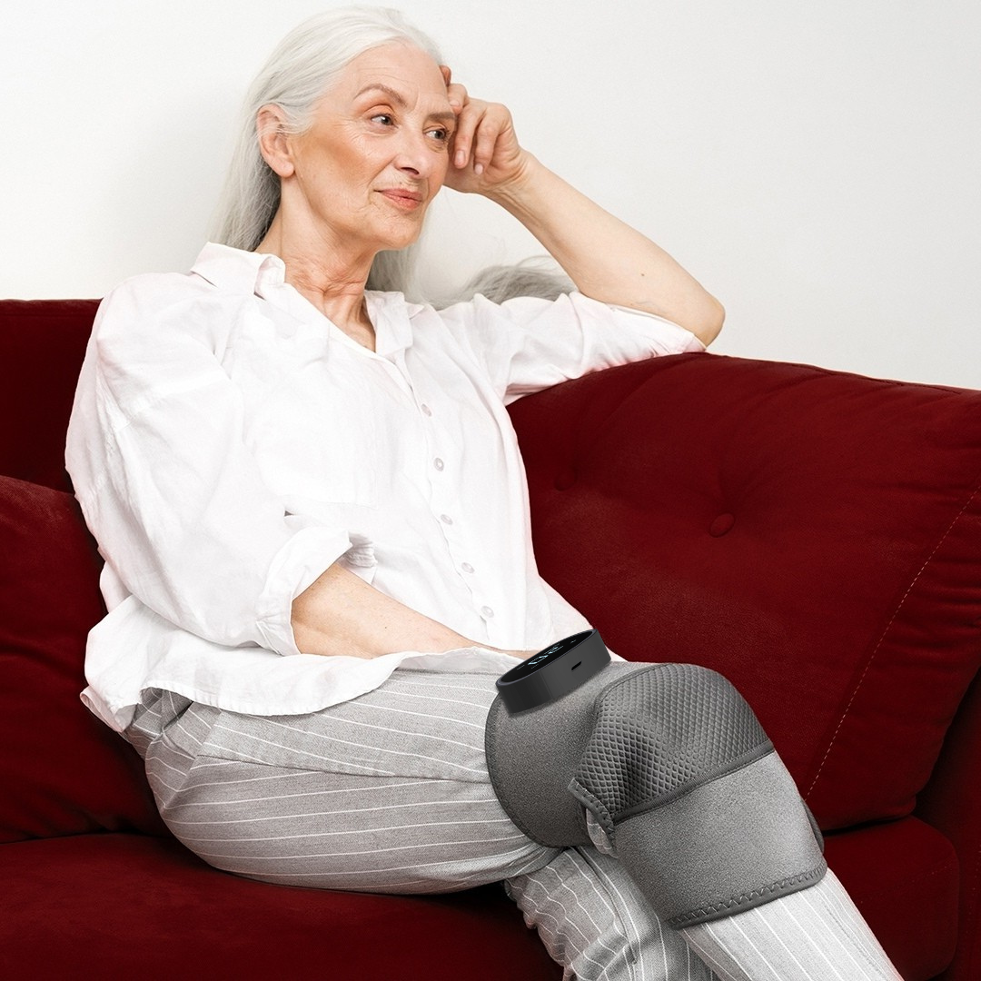 Woman sitting on red couch, wearing gray VibeKnee knee brace, feeling comfortable